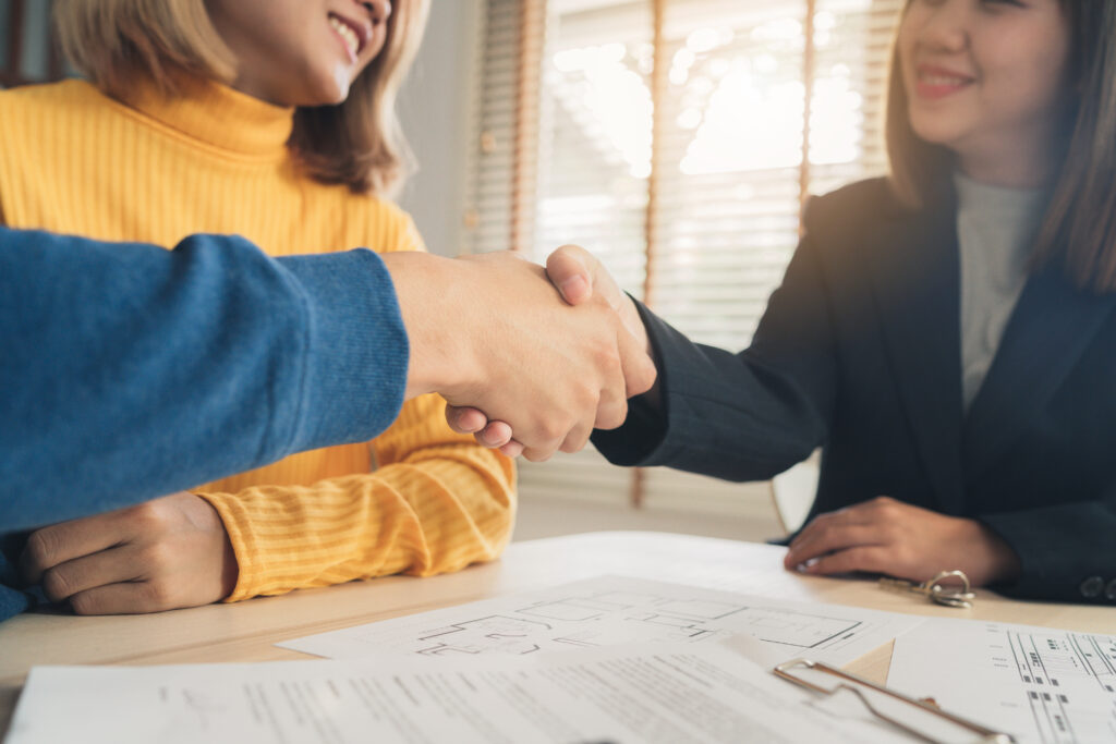 Sócios apertando as mãos com corretor de imóveis após assinar contrato de locação comercial.